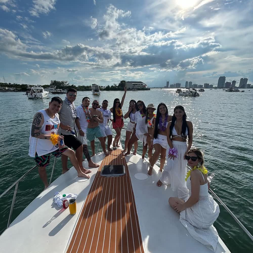 Invitados de pie en la proa de teca del Chris Craft, con las bebidas en la mano y el skyline de Miami detrás