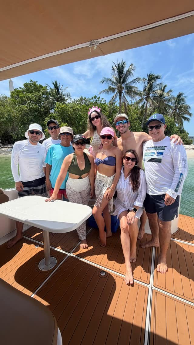 A group around the cockpit table on the teak deck, anchored off a palm-lined shore