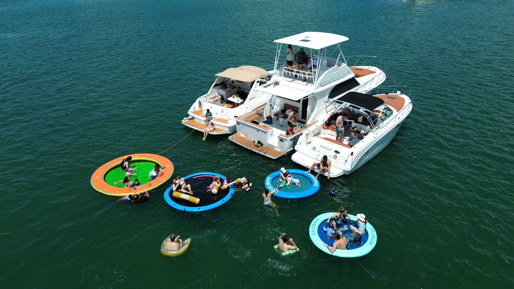 Los tres botes amarrados vistos de lado, con cuatro piscinas flotantes atadas y gente sentada en ellas