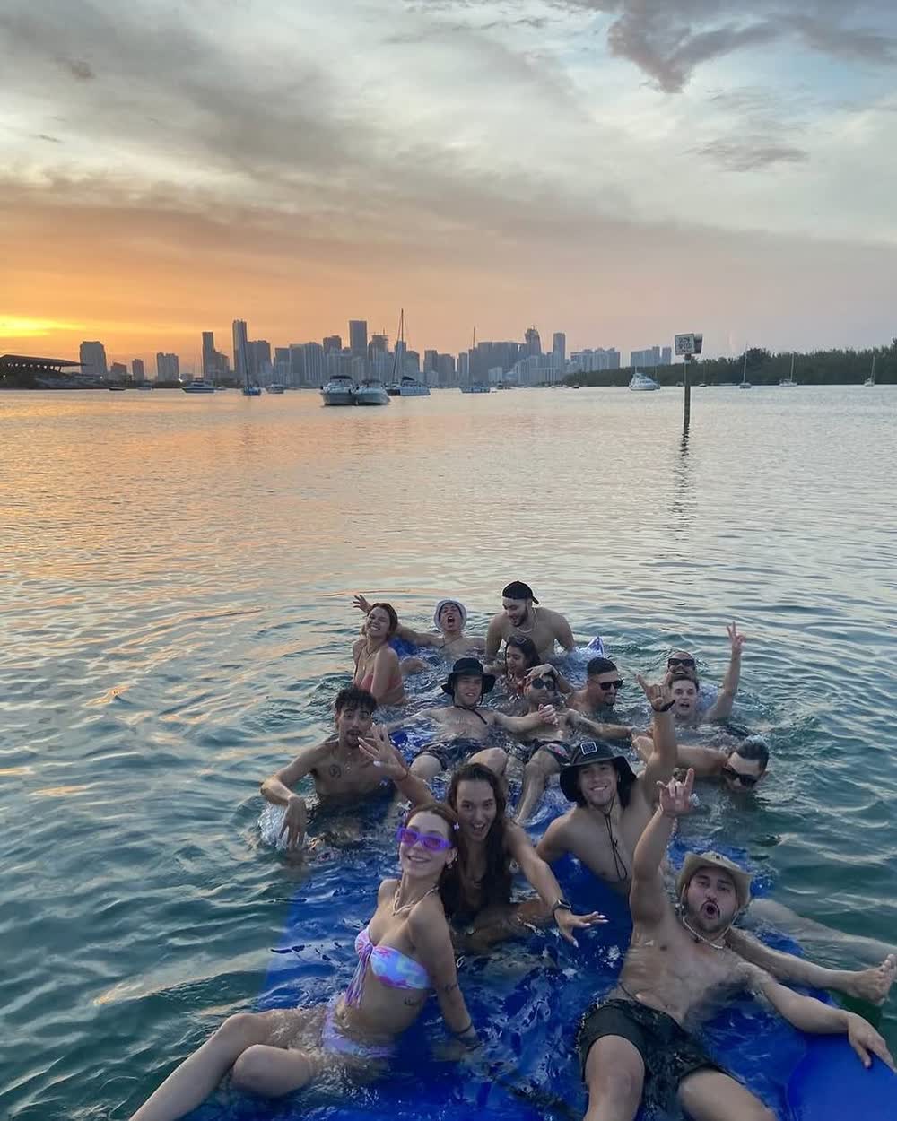 The group in waist-deep water at the sandbar as the light drops behind the city